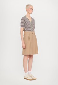 Striped short-sleeve top with buttons, paired with a pleated beige skirt featuring two front buttons. Worn with beige sneakers and white socks.