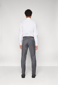 Chemise blanche à manches longues et pantalon gris sur mesure avec une coupe slim ; poches arrière plates ; chaussures noires brillantes.