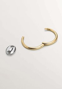 Pulsera de metal color dorado con un diseño suave y redondeado, acompañada de un broche ovalado plateado con dos orificios para el enganche.