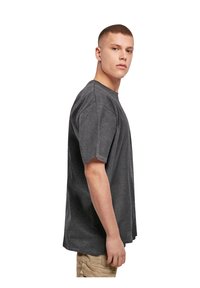 Mørkegrå bomulds t-shirt med rund hals, korte ærmer og løstsiddende pasform, vist fra siden mod en ensfarvet hvid baggrund.