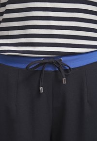 Black drawstring tied over blue waistband on black pants, paired with black and white horizontal striped top.