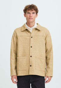 Beige wool blend jacket with a collar, front button closure, two large pockets, and tonal stitching. Fabric has a soft texture.