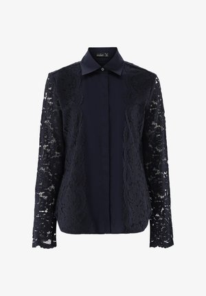 Navybluse mit klassischem Kragen, Knopfleiste und langen Spitzensäumen mit gewelltem Rand. Der glatte Stoff des Körpers kontrastiert mit der Spitzenstruktur.