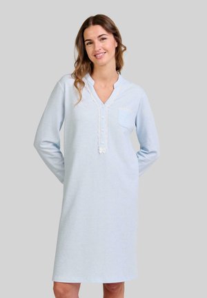 Mujer sonriendo con cabello ondulado que lleva un vestido de noche de manga larga y hasta la rodilla de color azul claro, con botones y detalles de encaje.