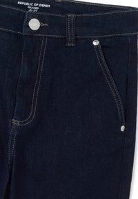 Pantalones vaqueros de mezclilla azul oscuro con un corte relajado, que cuentan con herrajes de plata, cierre de botón en la parte superior y diseño estándar de cinco bolsillos.