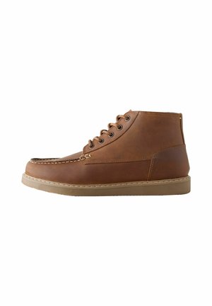 Botas de cuero marrón hasta el tobillo con punta redonda, seis ojetes para cordones, detalles cosidos y suela de goma en tono claro. Textura lisa con un brillo sutil.