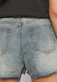 Shorts de mezclilla de un color azul claro deslavado, con dobladillo deshilachado y dos bolsillos traseros. Presenta costuras en contraste y un diseño de tiro medio.