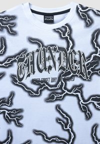 Koszulka z czarno-białym wzorem błyskawic, tekst w stylu gotyckim "THUNDER" oraz mniejszy tekst "Nigdy nie zapominaj, dlaczego to się zaczęło" z przodu.