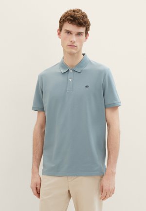Hele sinine polo-särk, mis on valmistatud puuvillast, koos kaelusega, kahe nööbiga ja lühikeste varrukatega. Rinna peal on väike tikandiga logo.