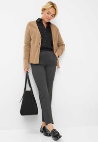 Cardigan beige con bottoni, blusa nera, pantaloni grigi sartoriali, mocassini neri e una borsa nera. Texture lisce e colori neutri.