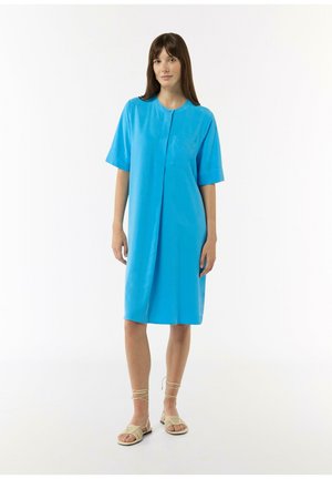 Blaues kurzärmeliges Kleid mit Knopfleiste, knielang, mit einer Brusttasche. Glatte Stoffqualität mit dezentem Glanz; Modell trägt beigen Sandalen.