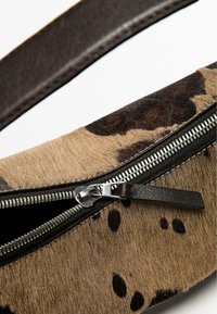 Brun och beige mönstrad väska med ett texturerat pälsliknande material, guldig dragkedja och ett kontrasterande mörkt läderrem. Slät inredning.