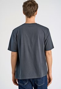 Harmaa lyhythihainen t-paita pyöreällä kaula-aukolla, valmistettu puuvillasta. Ominaisuuksina rento istuvuus ja suora helma, esitelty takaa.