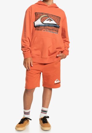 Set van een oranje hoodie en shorts van katoen, met een groot grafisch logo op de voorkant. De shorts hebben een logo-accent op het been.