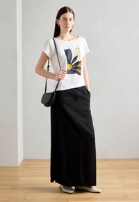 T-shirt blanc avec un graphique de fleur colorée, associé à une jupe maxi noire et un petit sac bandoulière noir. Tissu doux et coupe décontractée.