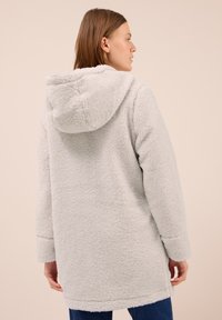 Manteau en polaire gris clair avec une coupe décontractée, capuche et manches longues, présentant une surface texturée et un ourlet arrière légèrement plus long.