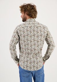 Langarmshirt met bloemenprint met witte, groene en roze bloemen op een lichte achtergrond, met een knoopsluiting en een golvende zoom.