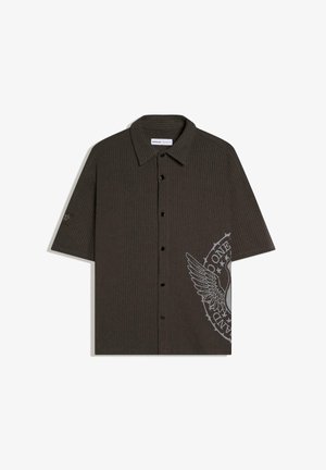 Tamno smeđa rebrasta košulja na kratke rukave s gumbima i ovratnikom te velikim krilatim grbom na donjoj desnoj strani.