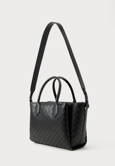 Černá kožená kabelka s prošívaným vzorem, dvěma krátkými uchy a jedním dlouhým nastavitelným ramenním páskem na bílém pozadí.