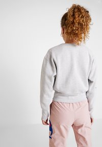 Sweatshirt gris avec une coupe confortable, épaules tombantes et poignets côtelés, associé à un pantalon rose clair avec un accent graphique bleu.
