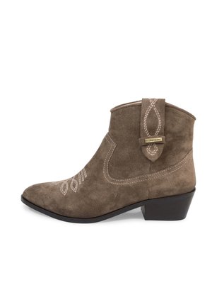 Boots en daim marron avec un petit talon noir, coutures blanches décoratives sur le côté et l’avant du pied, et languette avec étiquette sur la cheville extérieure.