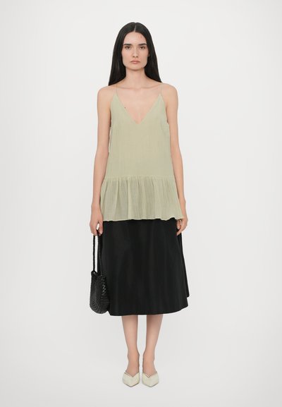 Light green, pleated tank top with a V-neck and a flared hem, paired with a black, ankle-length skirt. Accessories: a woven black handbag.