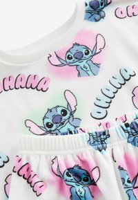 Fehér anyagú ruha, amelyén színes nyomatok láthatók Stitch-ről, "OHANA" felirattal, pasztell háttérrel és elasztikus derékkal.