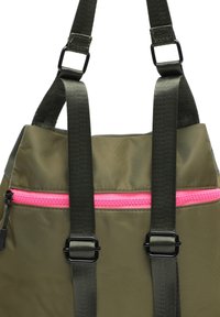 Sac à dos vert olive en tissu lisse, doté d'une fermeture éclair rose, de bretelles réglables et de ferrures noires. Le design est simple avec une forme structurée.