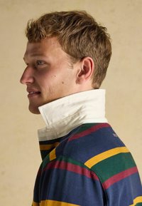 Rugbyshirt im Stil mit Streifen in Dunkelblau, Grün, Gelb und Burgunder, sowie einem weißen Kragen und strukturiertem Stoff.