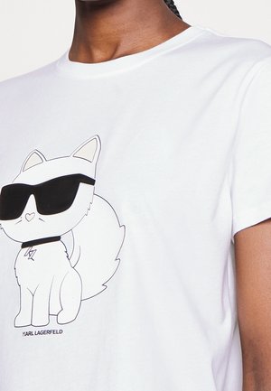 Biała koszulka z nadrukiem kartonowego lisa noszącego duże czarne okulary przeciwsłoneczne i obrożę, noszona przez osobę o ciemnej skórze i zaplecionych włosach.