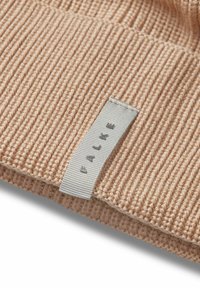 Cappello lavorato a maglia beige con texture a costine e etichetta argento con il nome del marchio "FALKE". Morbido filato e dettagli di design essenziali.