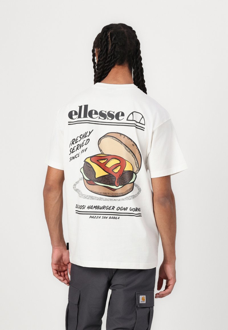 Camiseta blanca con un gráfico de una hamburguesa con una rebanada de queso amarillo y salsa roja. La parte posterior muestra el logo de "ellesse" y texto.