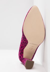 Chaussure à talon haut en léopard rose avec une texture douce, bout pointu et semelle beige. Présente un subtil branding sur la semelle intérieure.