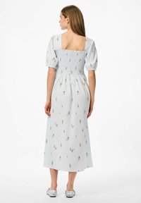 Kleita ar vieglu zilu teksturētu audumu, ar smockētu krūšu daļu un īsām pūkainām piedurknēm. Izmērcēta ar mazām ziedu detaļām.