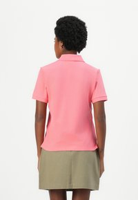 Korte mouwen polo shirt in felroze, gemaakt van glad stof. Heeft een klassieke kraag en een getailleerd ontwerp, gecombineerd met een groene rok.
