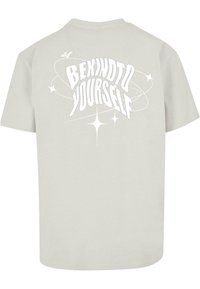 Lichtgrijze katoenen T-shirt met grote witte tekst "WEES VRIENDELIJK VOOR JEZELF" met decoratieve sterren en spiralen. Korte mouwen en een ronde halslijn.