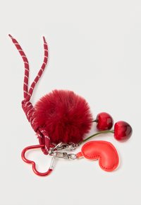 Μπρελόκ με κόκκινη φουντίτσα, διακοσμημένο με κούμπωμα σε σχήμα καρδιάς και μοτίβο από υφή κόκκινο δέρμα. Διαθέτει πλεγμένο λουράκι με λευκές ρίγες.