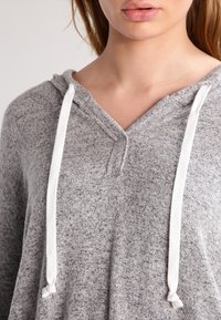 Sudadera gris hecha de tela suave, con un diseño de cuello en V, cordones blancos y un corte relajado. Texturizada con un patrón jaspeado.