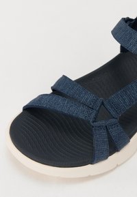 Blå stoffsandaler med flere justerbare stropper, en teksturert mørk såle og en lyst farget, polstret mellomsåle for komfort.