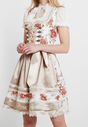 Un mannequin porte un dirndl blanc à fleurs avec des manches en dentelle, un corsage beige à lacets et un tablier en satin.