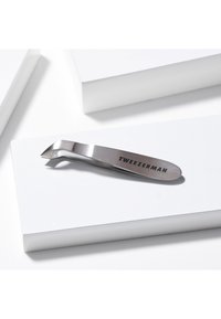 Pinzetta inclinata in acciaio inossidabile con marchio "TWEEZERMAN", appoggiata su un blocco rettangolare bianco.