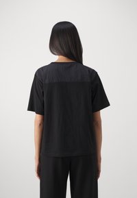 Svart t-shirt med kort ärm som har en sömlös design, med olika texturer på ryggen och axlarna. Slät tygfinish.