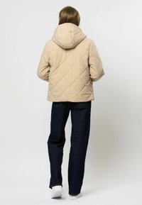 Béžová prešívaná puffa bunda s kapucňou, s diamantovým vzorom. V kombinácii s tmavými džínsovými nohavicami a bielymi teniskami.