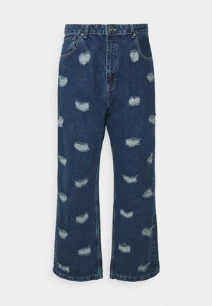 Jeans de denim em azul escuro com um corte largo, cintura alta e vários remendos desgastados com bordas esfiapadas.