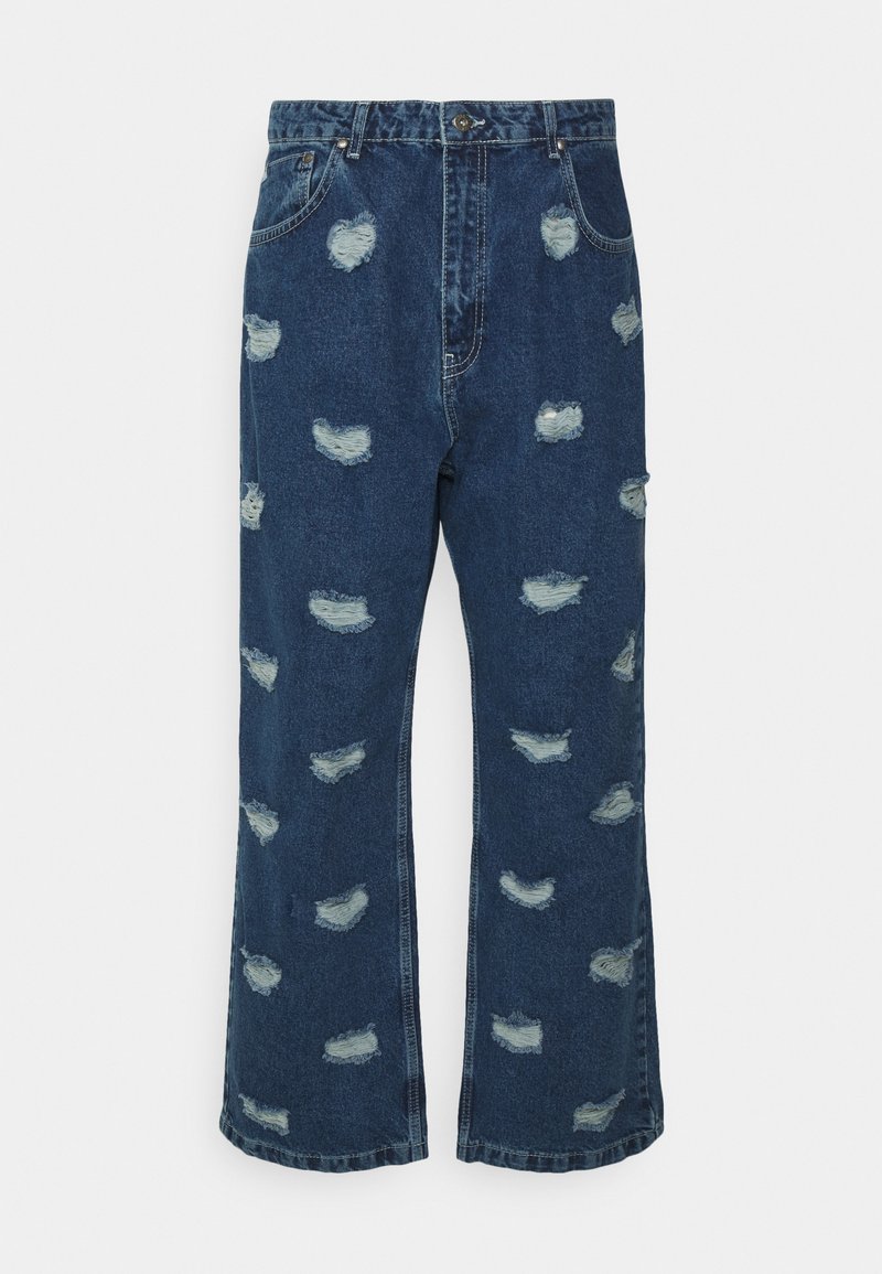 Jeans de denim em azul escuro com um corte largo, cintura alta e vários remendos desgastados com bordas esfiapadas.