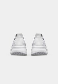 Weiße Sportschuhe mit einer strukturierten Sohle, schlankem Design und verstärktem Absatz. Mit dezenten grauen Akzenten und einem Markenlogo auf der Rückseite.