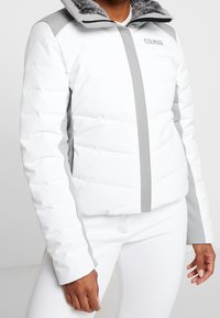 Vit isolerad jacka med grå detaljer, som har hög krage och dragkedjestängning. Fodra med vadderad design och mjukt, texturerat innerfoder.