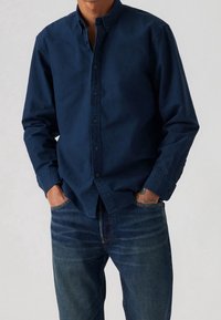 Granatowa koszula zapinana na guziki, wykonana z lekkiego materiału, z klasycznym kołnierzem i długimi rękawami, zestawiona z ciemnymi dżinsami.