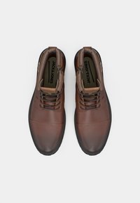 Botas de cuero marrón con cordones y cremalleras laterales, suelas negras y el logotipo "JACK & JONES" en el interior del cuello acolchado.