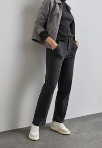 Jean noir en denim taille haute avec une coupe droite, poches avant, associé à une veste grise texturée et des baskets blanches.